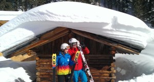 Zwei Skifahrer stehen vor einer tief verschneiten Holzhütte (Skigebiet Hochzeiger)