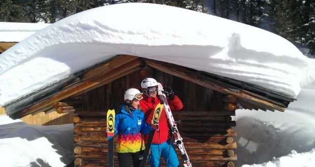 Zwei Skifahrer stehen vor einer tief verschneiten Holzhütte (Skigebiet Hochzeiger)