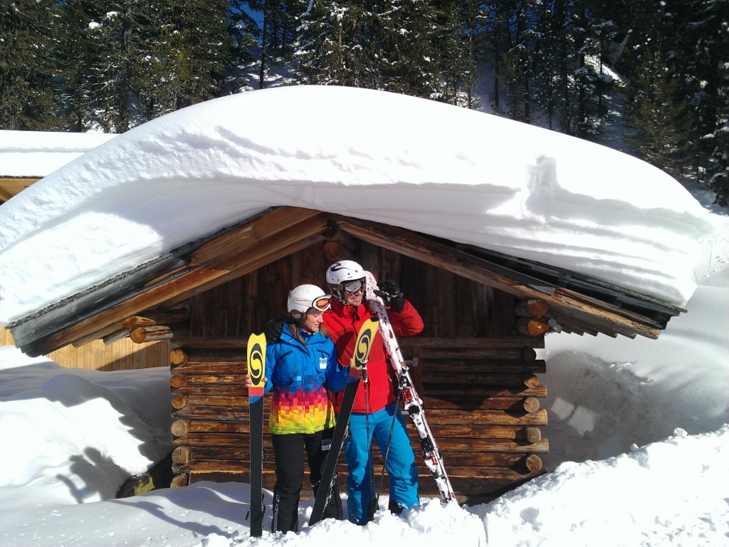 Zwei Skifahrer stehen vor einer tief verschneiten Holzhütte (Skigebiet Hochzeiger)